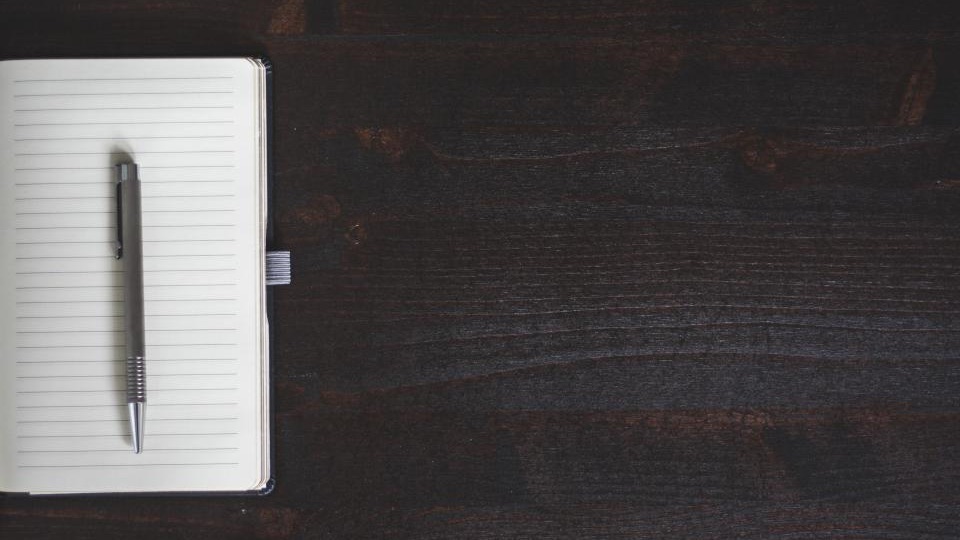 Open lined notebook with a silver pen on a dark wooden desk