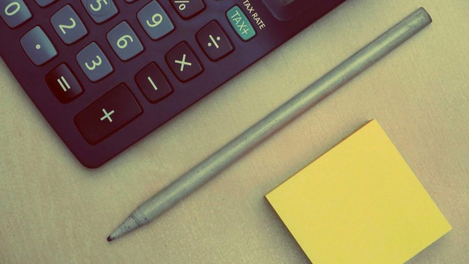 Close-up of a dark desk calculator beside a grey pencil and a yellow sticky note
