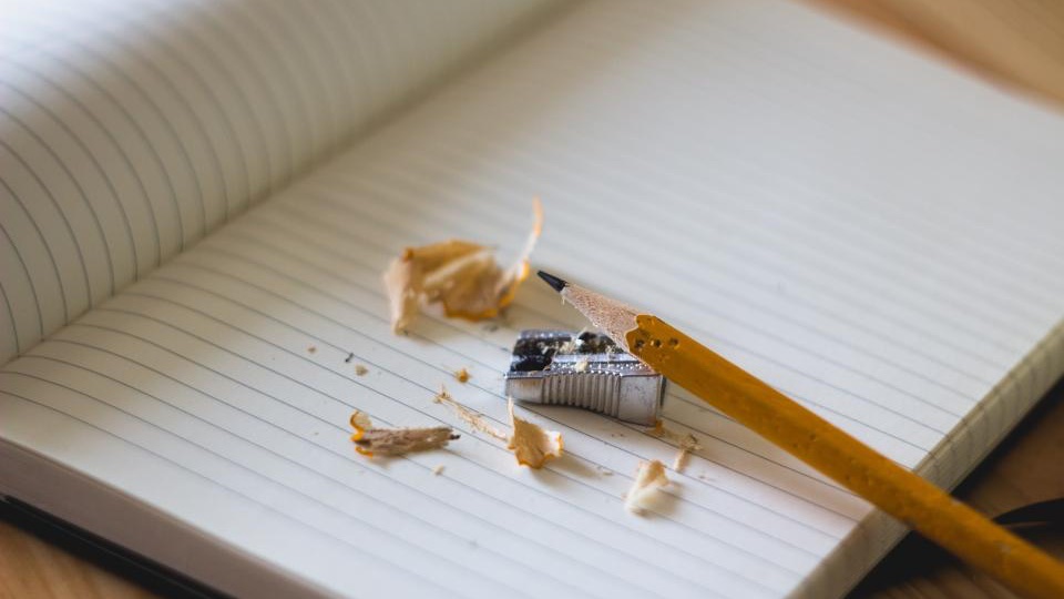 Open lined notebook with a pencil and pencil shavings on a wooden desk
