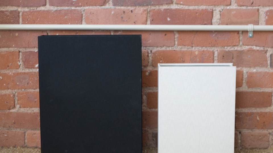 Two closed ring binders, one black and one white, standing against a brick wall