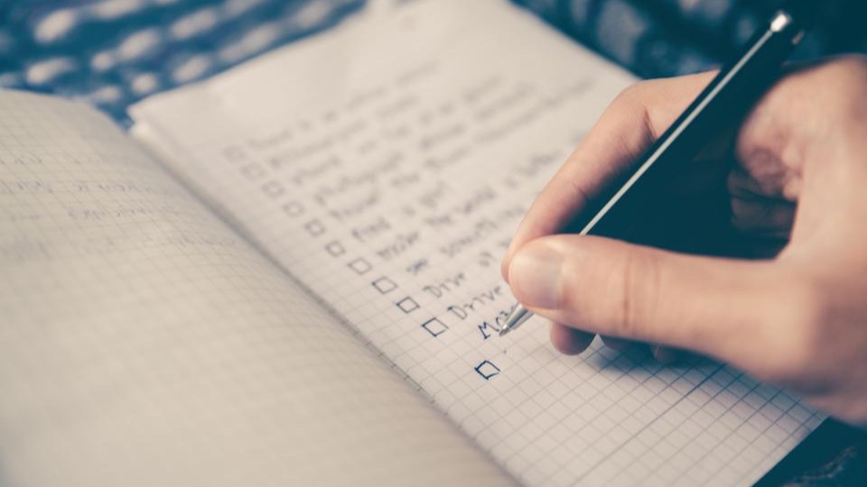 Hand writing a checklist with empty tick boxes in a squared notebook